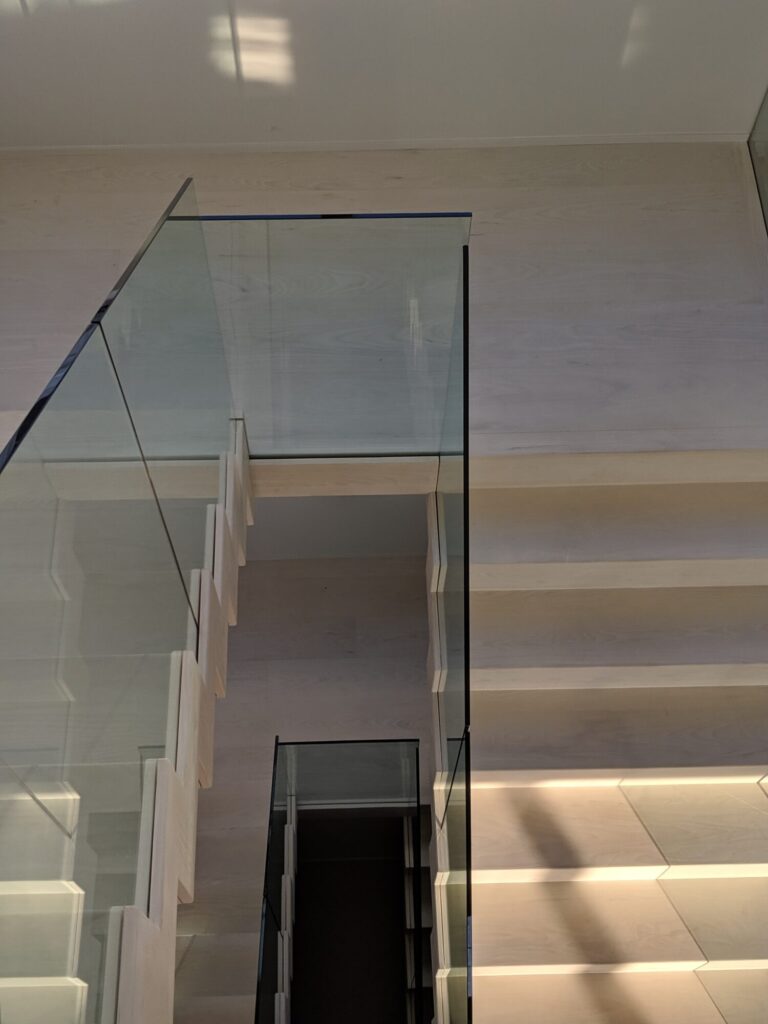 Modern zig zag stair with glass panels and satin black metal rails, photo 2 of 9